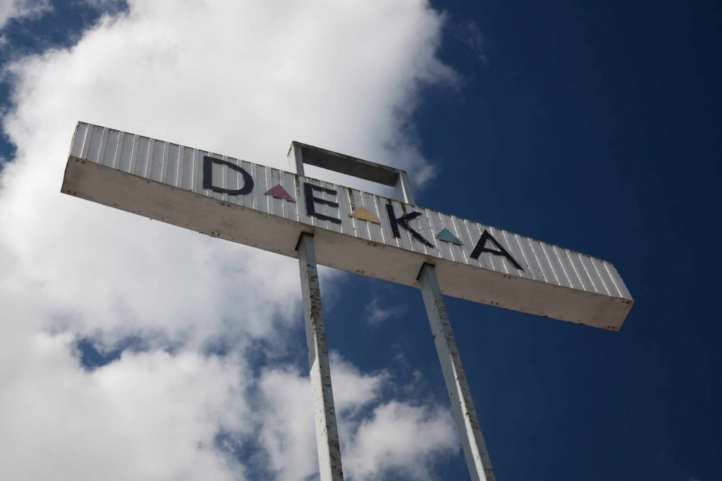The DEKA sign in Huntly, a long white sign spelling D E K A with coloured triangles, against a blue sky.
