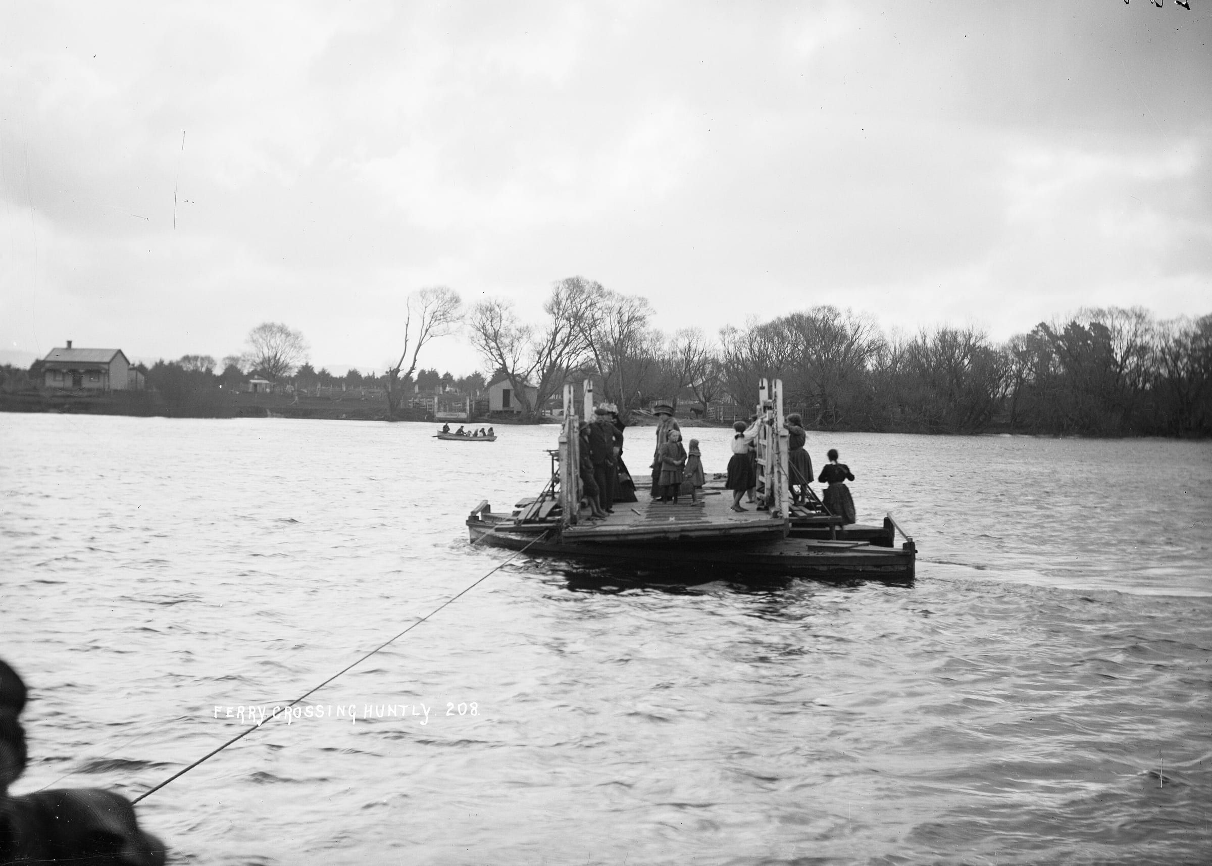 Black and white photo of a punt ferry carrying women and children across the Waikato River at Huntly.
