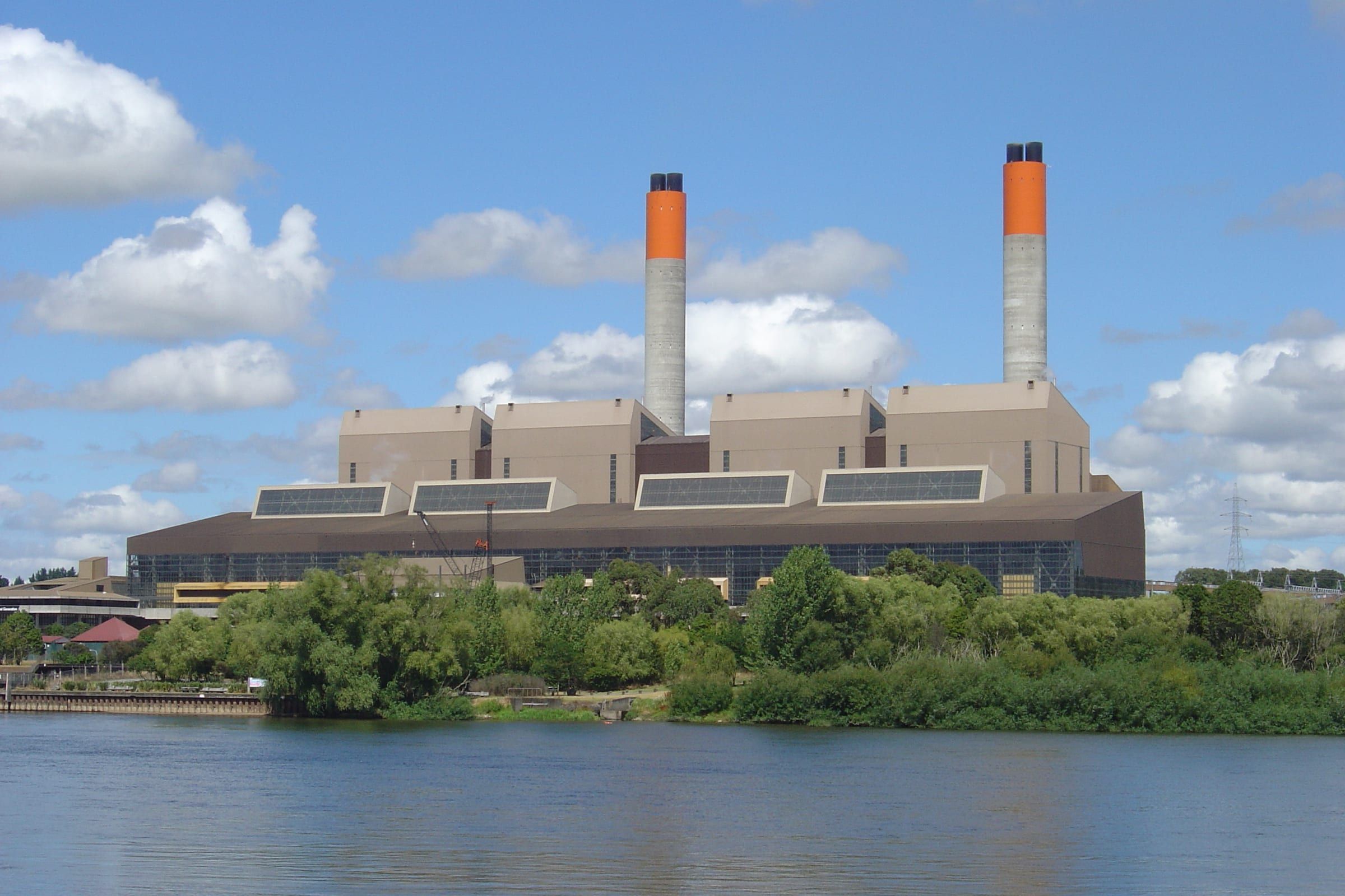 Huntly Power Station across the Waikato River, with its two tall chimneys painted orange at the top.